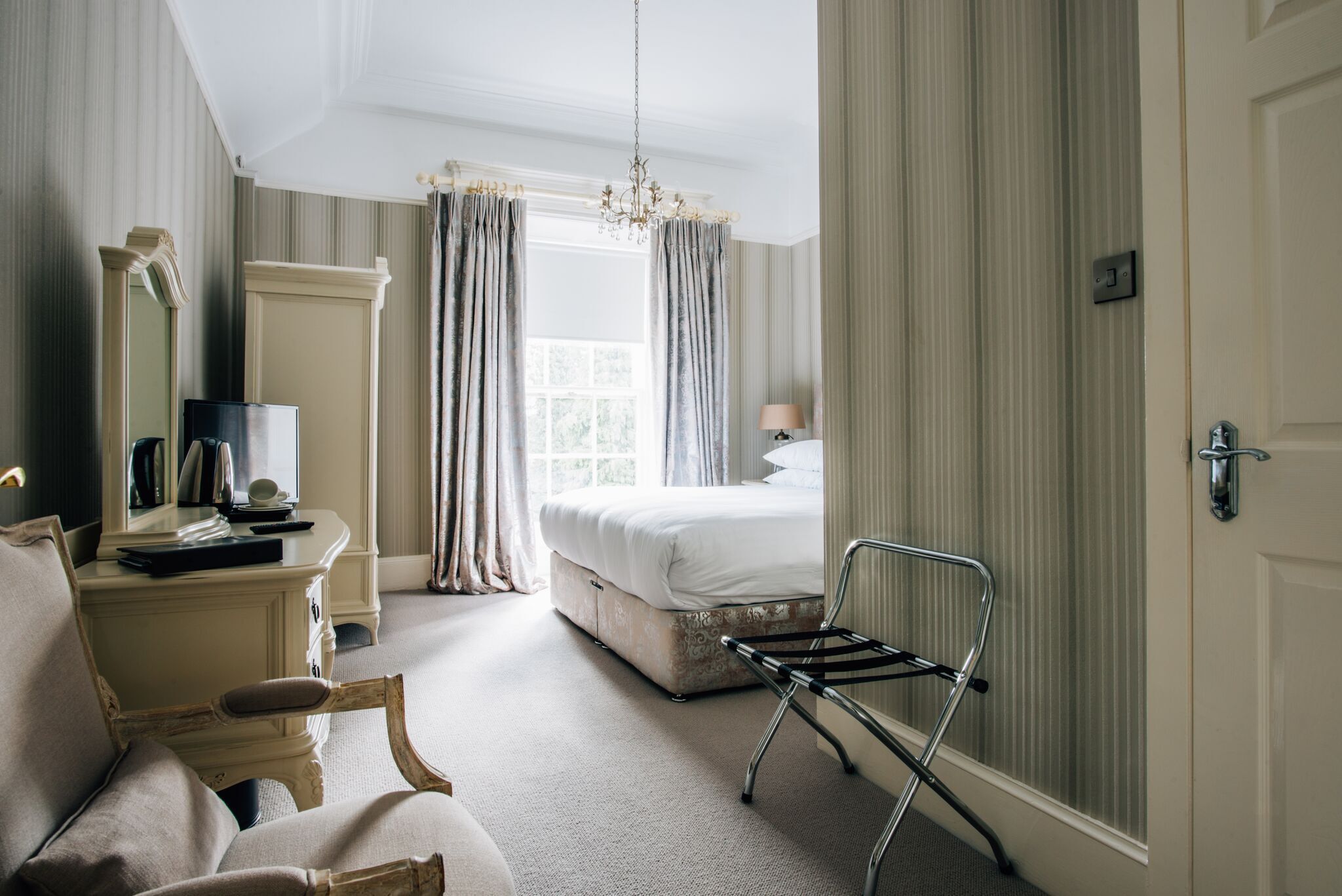 A hotel room with a bed, a desk with a mirror, a chair, and a window with curtains.
