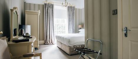 A hotel room with a bed, a desk with a mirror, a chair, and a window with curtains.