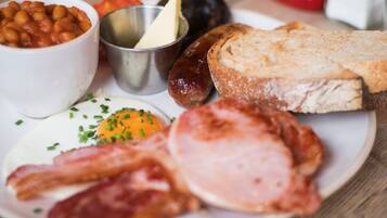 Ein Teller mit Speck, Eiern, Bohnen, Wurst, Toast und einer kleinen Butterportion.
