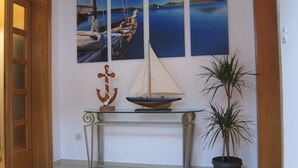 A hallway with a glass-top table displaying a model sailboat and an anchor, flanked by three maritime-themed paintings on the wall. - Cozy Stay Apartments (Dubrovnik)
