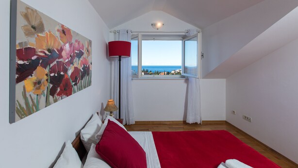 A bedroom with a bed, a window with curtains, a painting, and a lamp. - Cozy Stay Apartments (Dubrovnik)