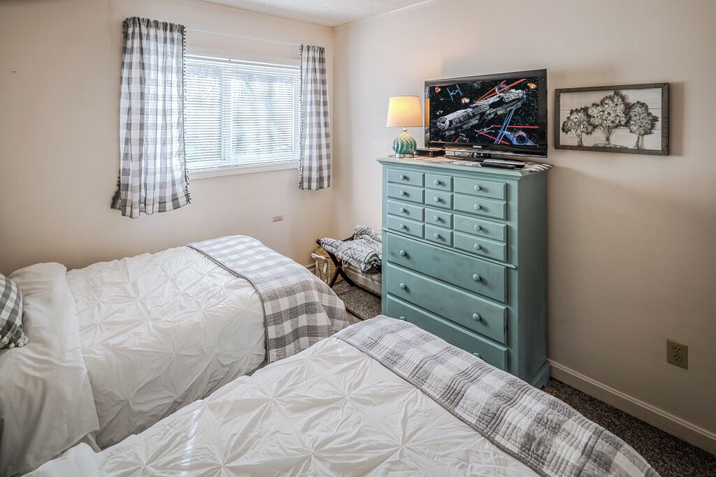 Una camera da letto con due letti, una cassettiera, una televisione e una finestra con tende.