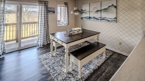A dining area with a wooden table and bench, a pendant light, and a view through a glass door to the outdoors. - Sugar Ski Comfort Two Bedroom - Unit 625 (Sugar Mountain)