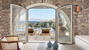 Una habitación con pared de piedra, puerta de cristal que da a una zona de piscina y vistas al mar.