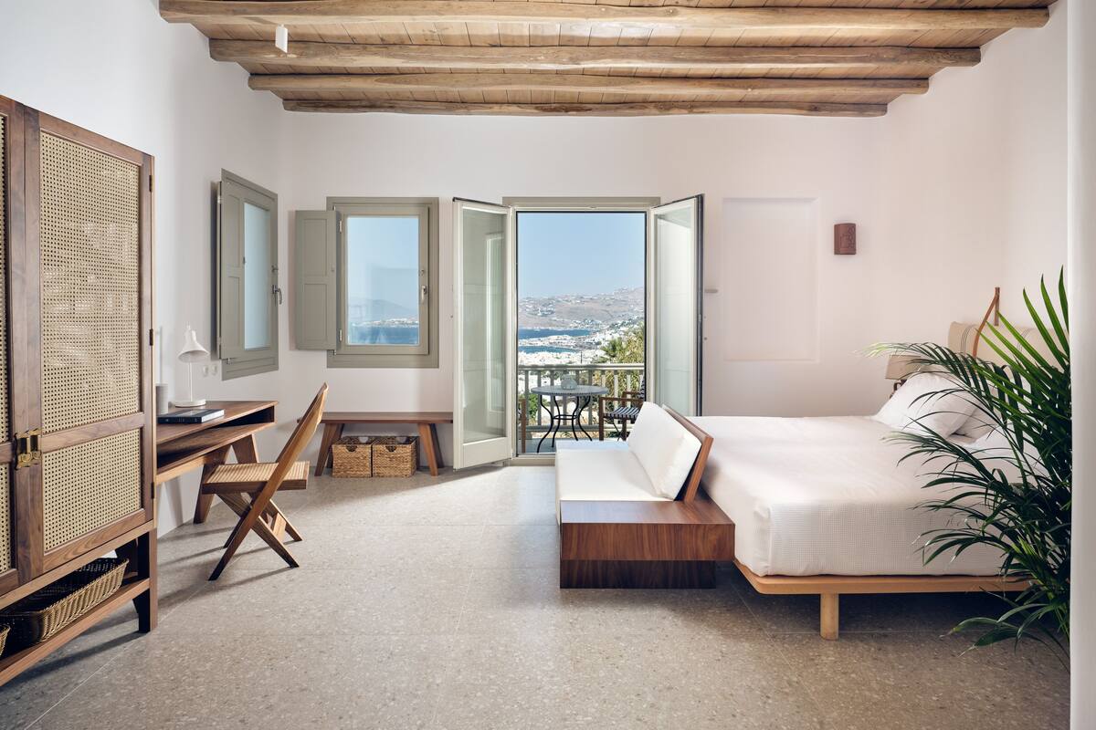 Une chambre avec un lit, un bureau, une chaise et un balcon ouvert donnant sur un paysage agréable.