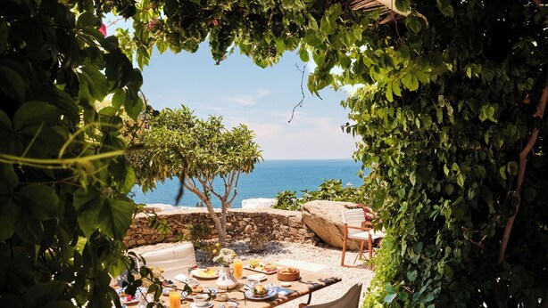 Un espacio de comedor al aire libre con una mesa preparada para una comida, con vistas a la playa y al mar.