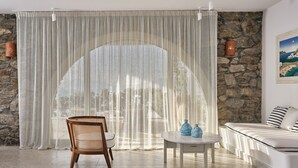 Una habitación moderna con pared de piedra, una silla de mimbre, una mesa redonda con jarrones y una cama con almohadones a rayas.