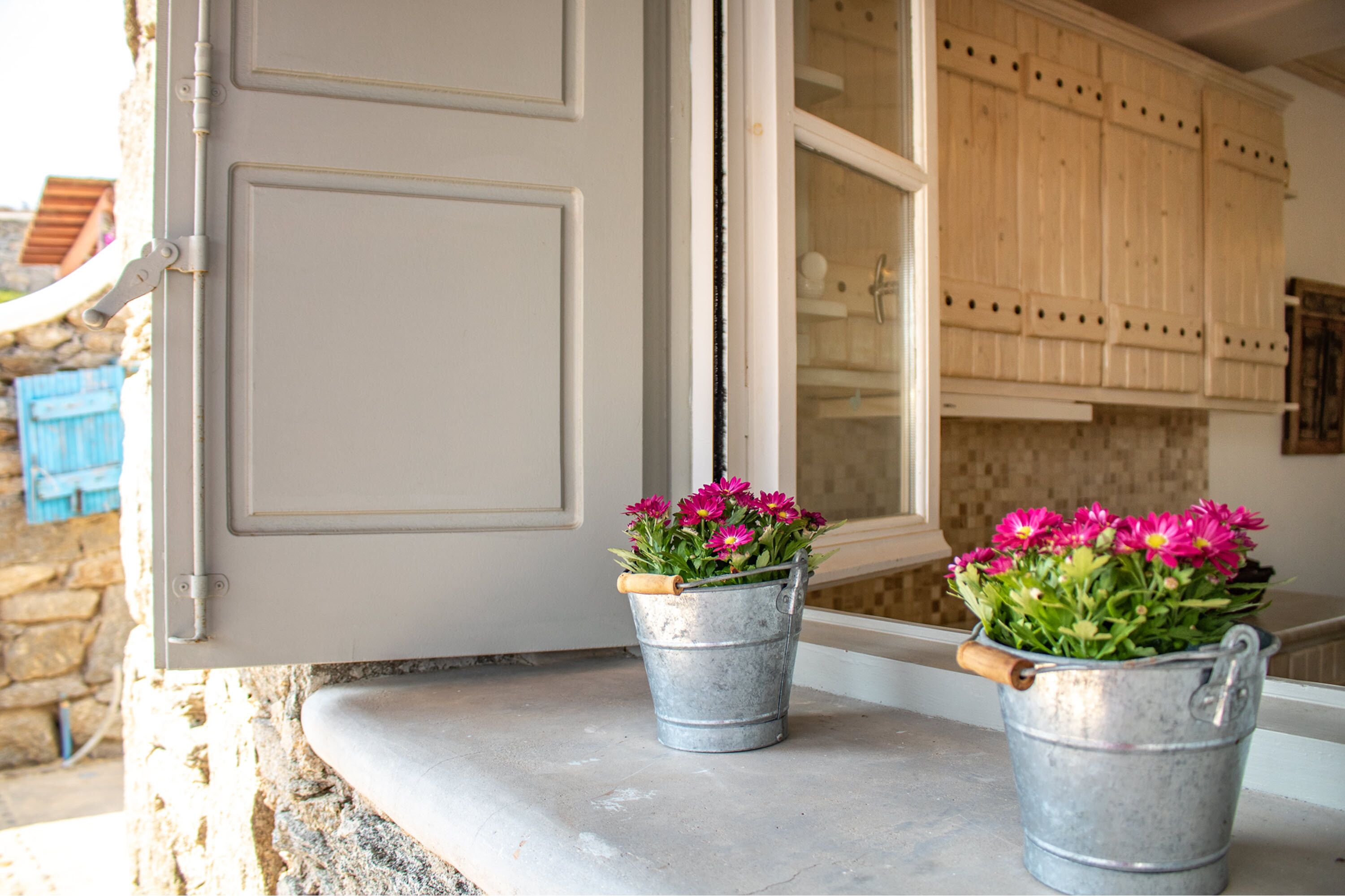 A kitchen with wooden cabinets and a window. There are two metal buckets with flowers on the windowsill.