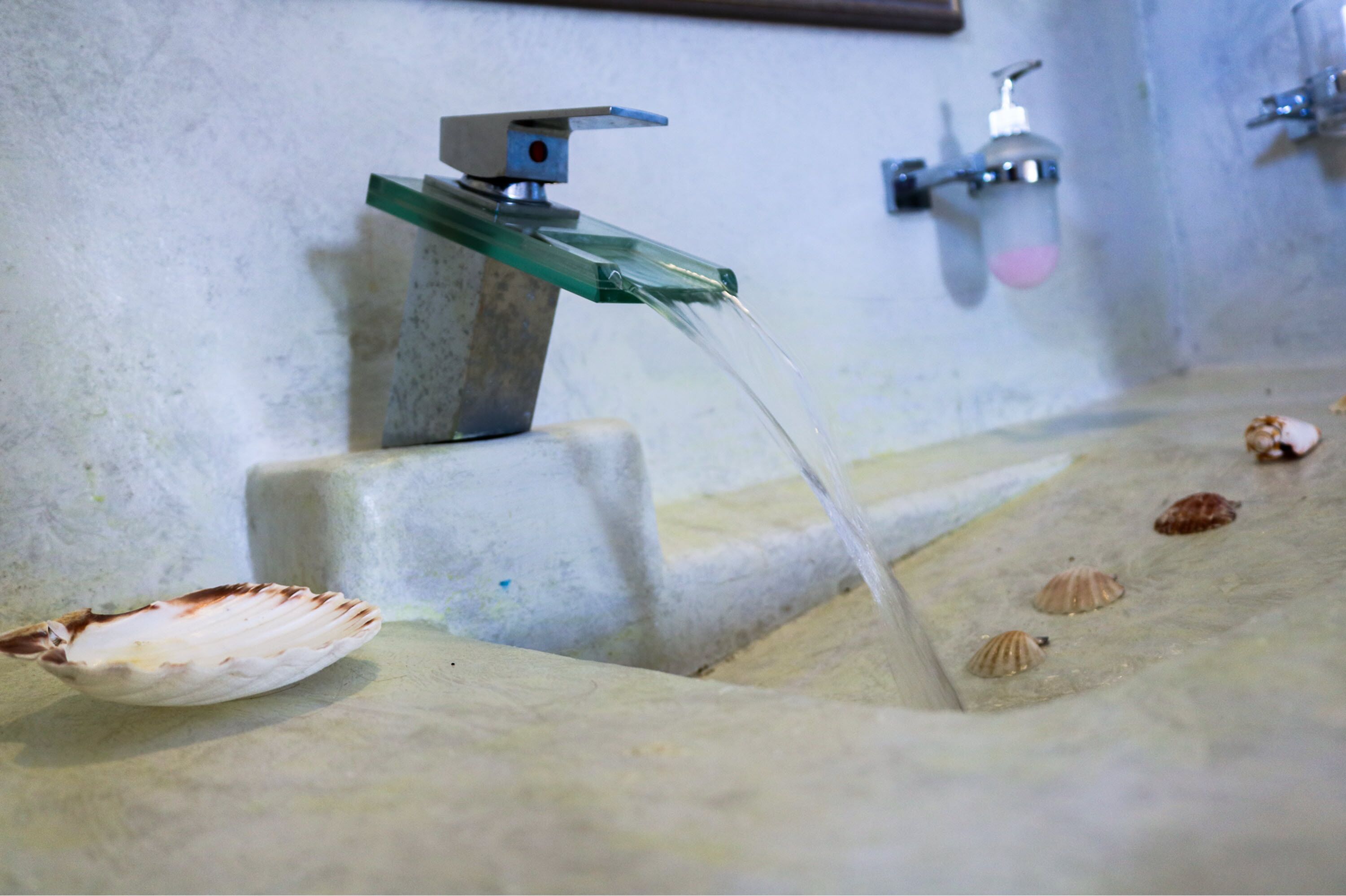 A bathroom with a glass-finished sink, a faucet, and seashells on the floor.