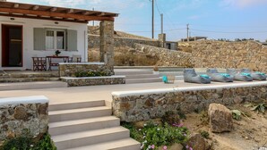 A stone house with a wooden porch, outdoor seating, and a stone staircase leading to the entrance. - Ortus Light Blue Mykonian Luxury Villa (Mykonos)