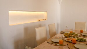 A dining table set with plates, glasses, and fruit, with a wall-mounted light above. - Ortus Light Blue Mykonian Luxury Villa (Mykonos)
