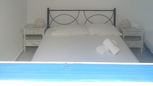 A bedroom with a bed, two bedside tables, a wall-mounted artwork, and a view of the sea. - Gorgeous Mykonian Studio DT Ornos (Mykonos)