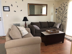 A living room with two sofas, a coffee table, a lamp, and wall decorations including a mirror and a tree decal. - Luxurious Mountain Vacation Rental Studio-Style Condominium Sleeps 3 (Sugar Mountain)