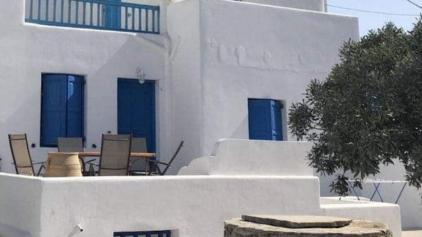 A white building with blue doors and windows, a stone bench, and a tree in the background. - Cycladic Studio - 4People DT Ornos (Mykonos)