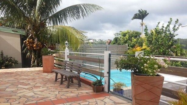En stenbelagt terrasse med bænk, pool og plantekasser.
