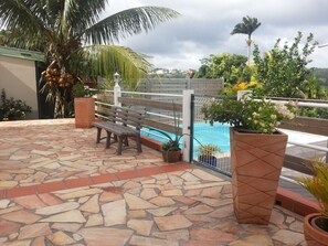Une terrasse en pierre avec un banc, une piscine et des plantes en pot.
