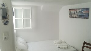 Ein kleines, schlichtes Zimmer mit einem Bett, einem Fenster, einem Bild und einem Stuhl.