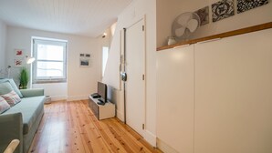 A modern living room with a wooden floor, a grey sofa, a small table with a TV, and a large fan on the wall.