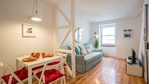 A modern living room with a dining area, wooden flooring, a grey sofa, and a white TV stand.