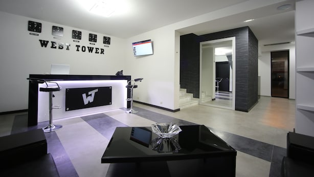 A reception area with a counter, bar stools, a digital screen, and a staircase leading to an upper level. - West Tower Hotel (Kutaisi)