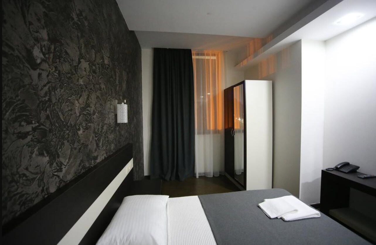 Habitación de hotel moderna con una cama grande, un escritorio con teléfono y vistas a la ciudad a través de una ventana.