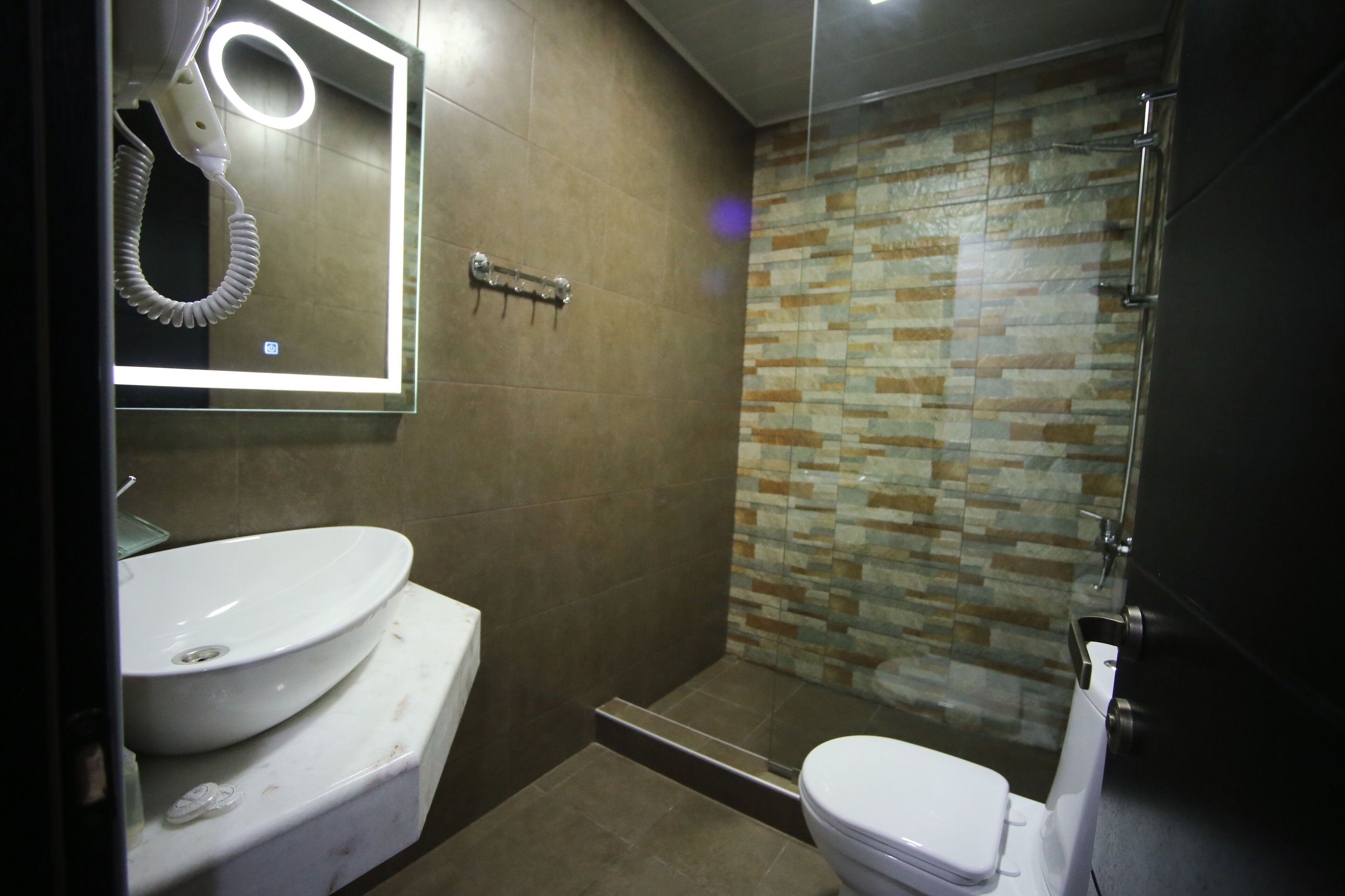 Un baño con un lavabo blanco, un espejo, un secador de pelo portátil y una ducha con pared de azulejos.