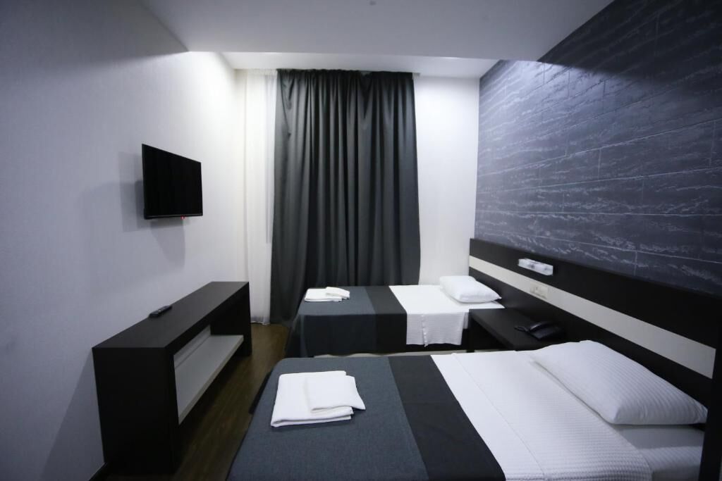 Habitación de hotel con dos camas, un televisor de pantalla plana montado en la pared, un escritorio con una silla y un ventanal con cortinas.