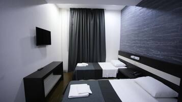Habitación de hotel con dos camas, un televisor de pantalla plana montado en la pared, un escritorio con una silla y un ventanal con cortinas.