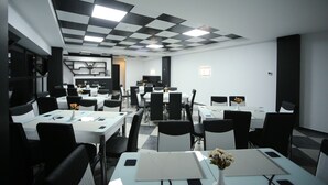 A modern dining area with checkered ceiling tiles, white tables, and black chairs. - West Tower Hotel (Kutaisi)