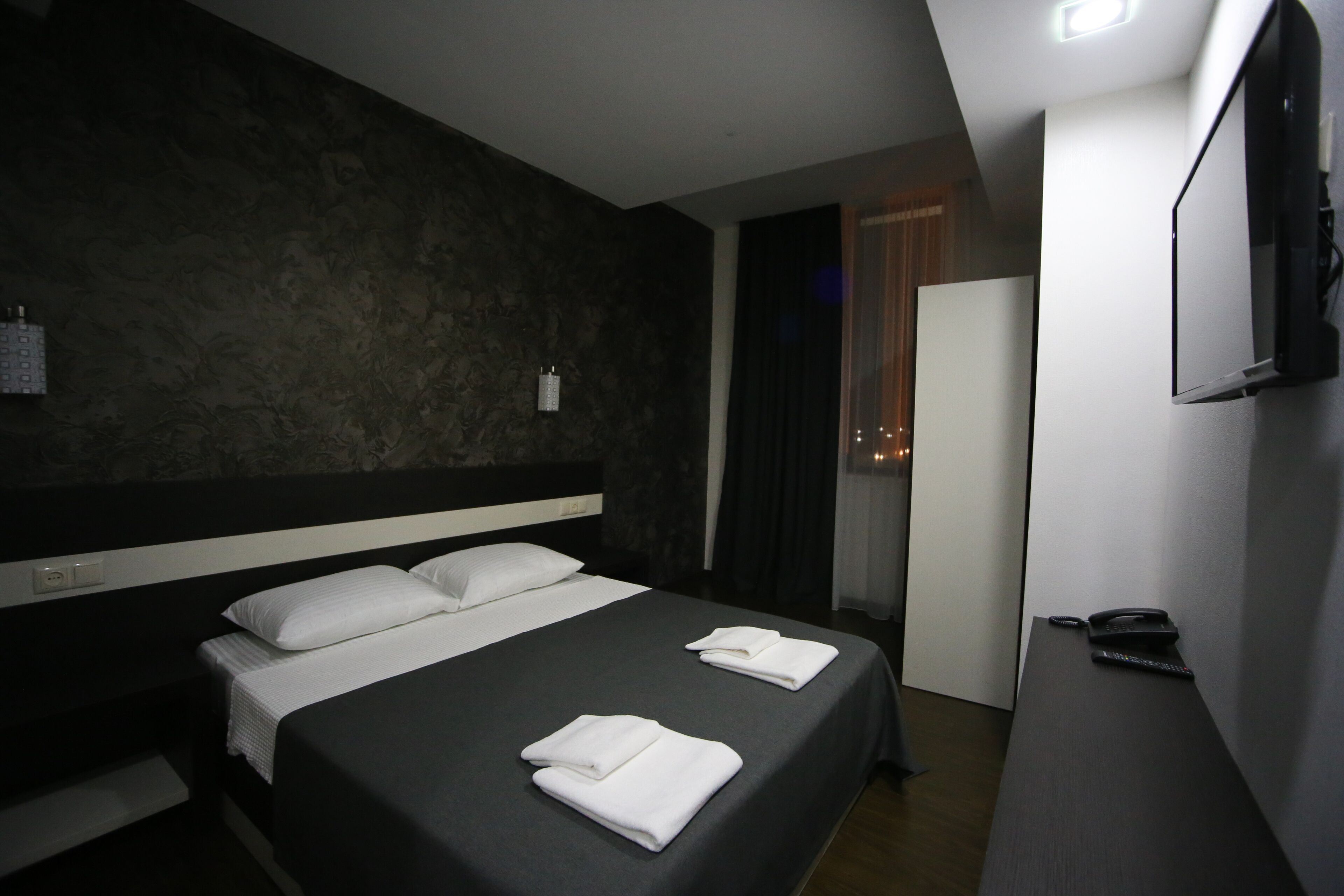 A hotel room with a large bed, a bedside table with a phone, and a wall-mounted TV.