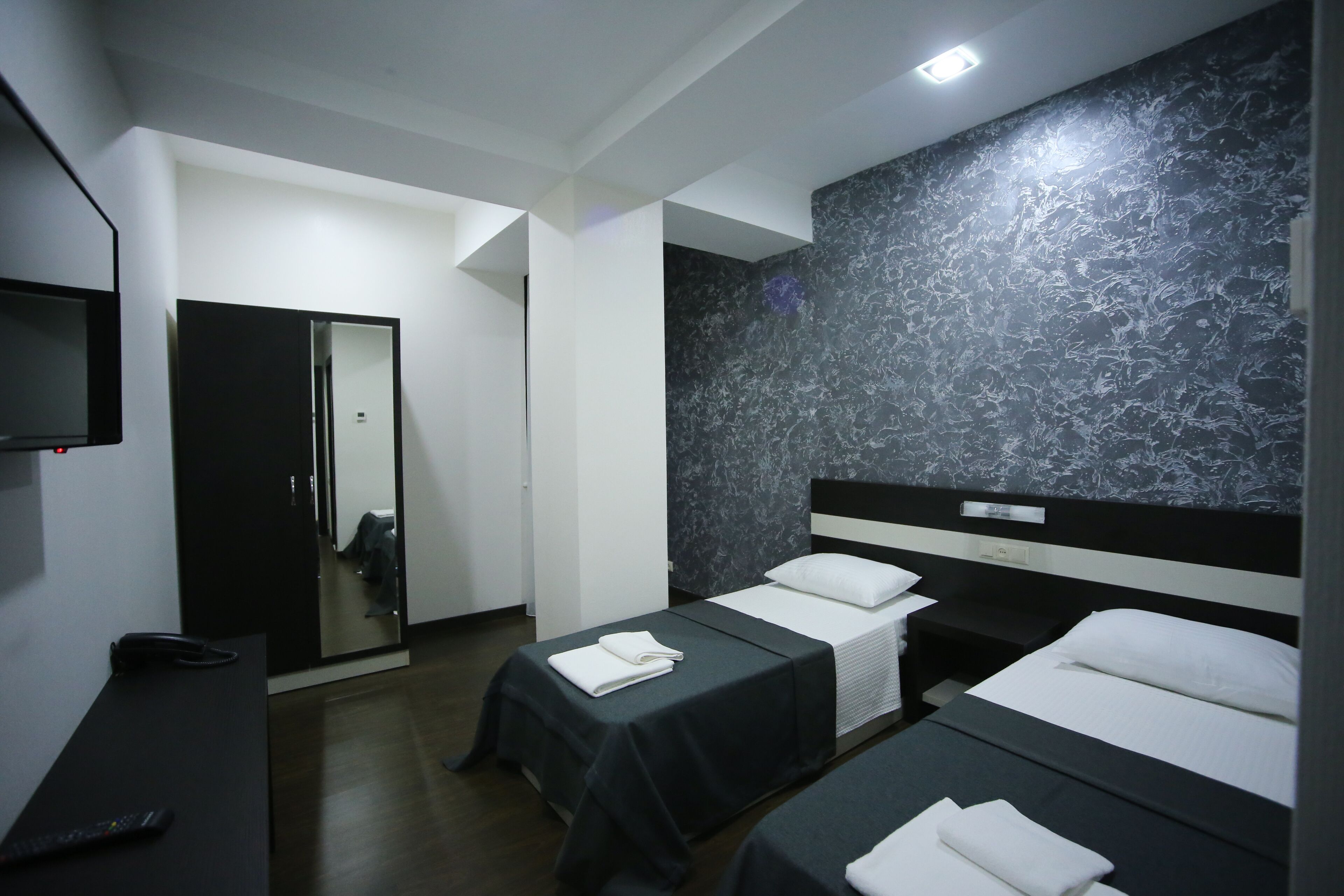 A hotel room with two single beds, a desk, a mirror, and a wardrobe.