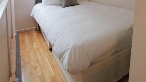 Ein Schlafzimmer mit Bett, Holzboden, Kopfteil und Wandleuchte.