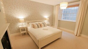 Een slaapkamer met een bed, twee nachtkastjes met lampen, een raam met gordijnen en een wand met een bloemenpatroon.
