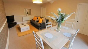Een woonkamer met een bank, salontafel en een eettafel met stoelen.