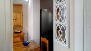 A compact kitchen with a wooden table, chairs, a black refrigerator, and a decorative white partition.