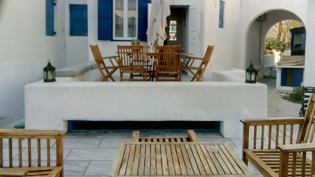 A white building with blue shutters and a wooden table and chairs in front.