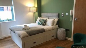 Un dormitorio ordenado con una cama, una lámpara de noche y una silla verde.