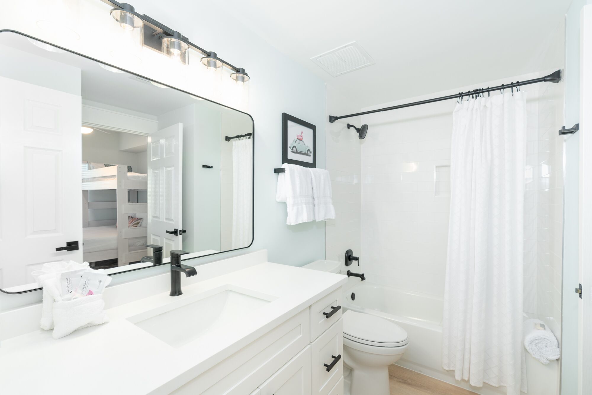 Un baño moderno con un lavabo blanco, espejo y inodoro. Se ve una cortina de ducha y un perchero.