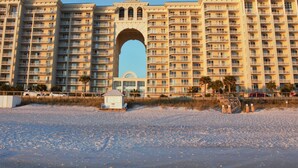 Un gran hotel con varios pisos, un arco central y una playa al frente.