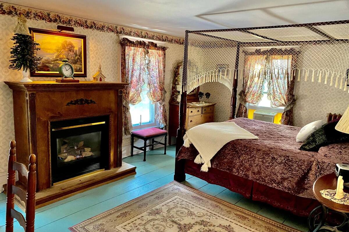 Une chambre à coucher avec un lit à baldaquin, une cheminée et une grande fenêtre avec des rideaux.