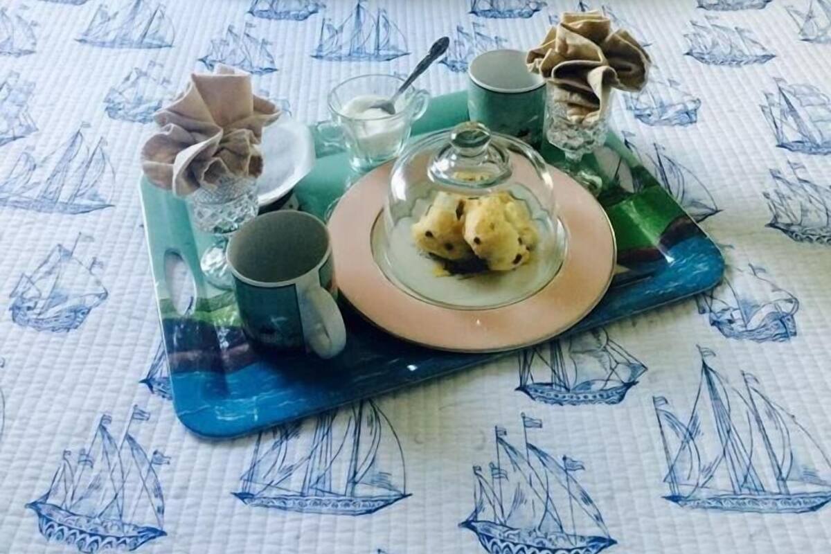 Un plateau de petit-déjeuner soigneusement disposé sur un lit agrémenté d’une couverture et de coussins aux motifs de voiliers.