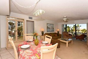 Enjoy meals together at the dining table for two, surrounded by a sofa and a painting, with a balcony offering a view of palm trees.