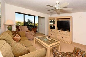 Relax in this stylish living room with a sofa, coffee table, and TV on a wooden cabinet, offering a view of palm trees and buildings outside.