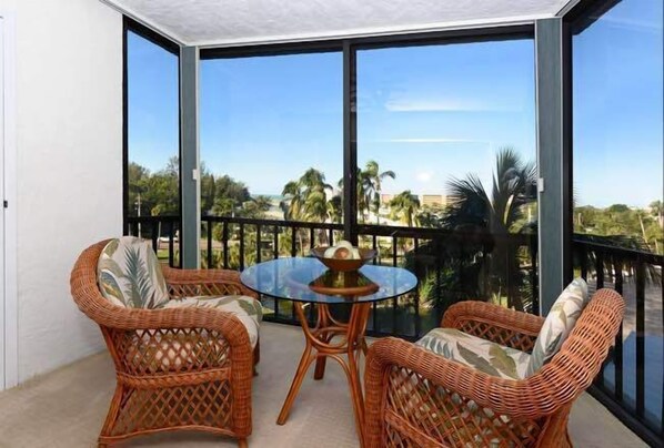Relax on the balcony with wicker chairs and a small table, taking in the view of palm trees and the surrounding landscape.