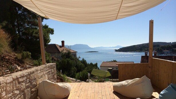 A wooden deck with two lounge chairs and a canopy, overlooking a coastal landscape with houses and a body of water. - Eco apartments Sunshine - Dance Lovers for 4 (Lumbarda)