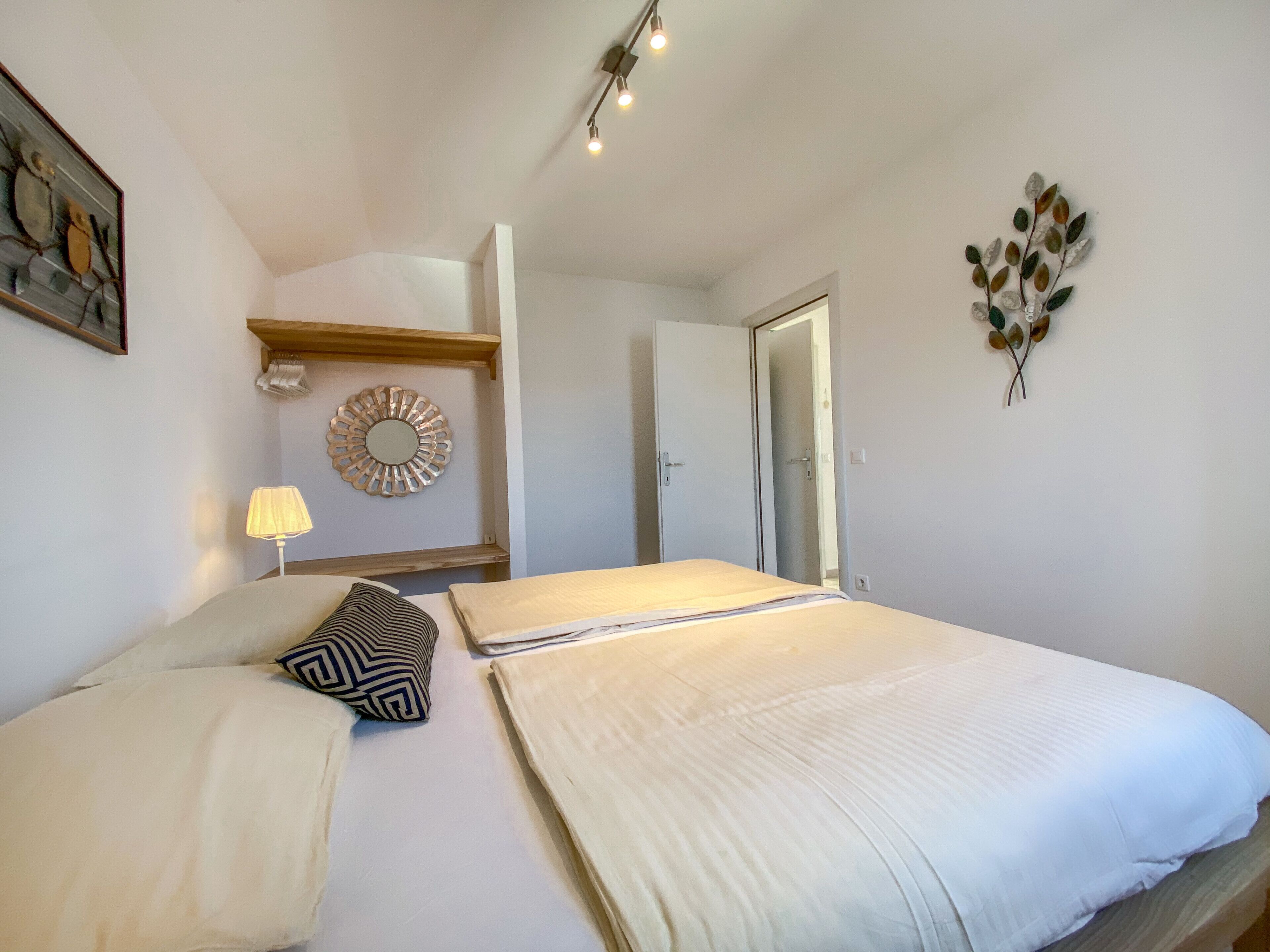 A bedroom with a large bed, a bedside lamp, a decorative mirror, and a wall-mounted artwork.