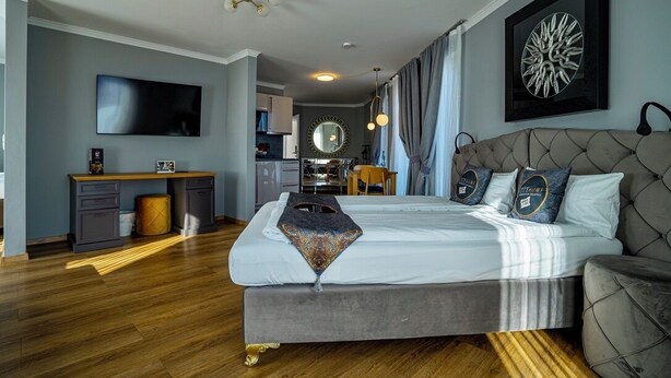 Un dormitorio moderno con una cama grande, un escritorio con televisor de pantalla plana y una zona de comedor visible a través de una puerta abierta.