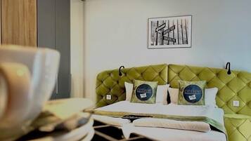 Una habitación de hotel con un cabecero verde tapizado, una cama con sábanas blancas, un cuadro enmarcado con una vista urbana y una lámpara de techo.