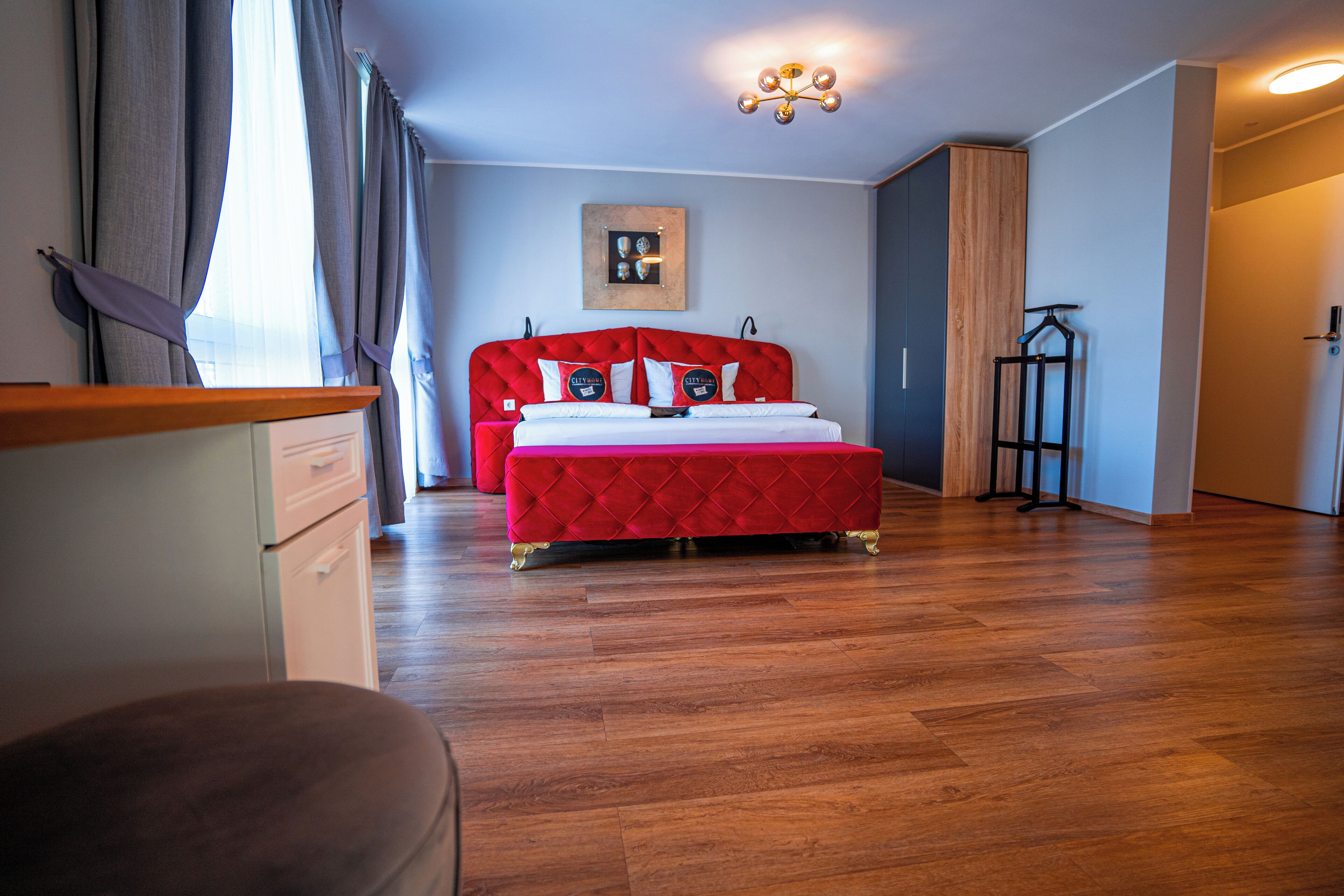 Een slaapkamer met een rode bed, houten vloer, een lijst met afbeelding aan de muur, en een hanglamp.