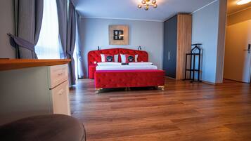 Ein Schlafzimmer mit einem roten Bett, Holzboden, einem gerahmten Bild an der Wand und einer hängenden Leuchte.